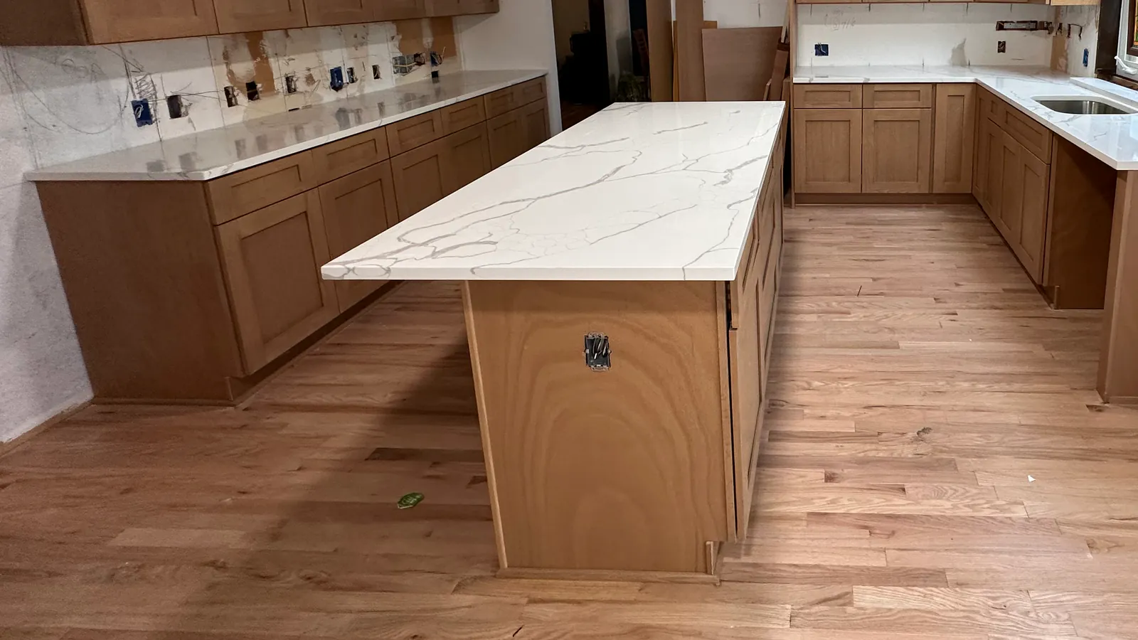 A calacatta-pattern quartz island on new red oak hardwood, the grain running the length of the kitchen