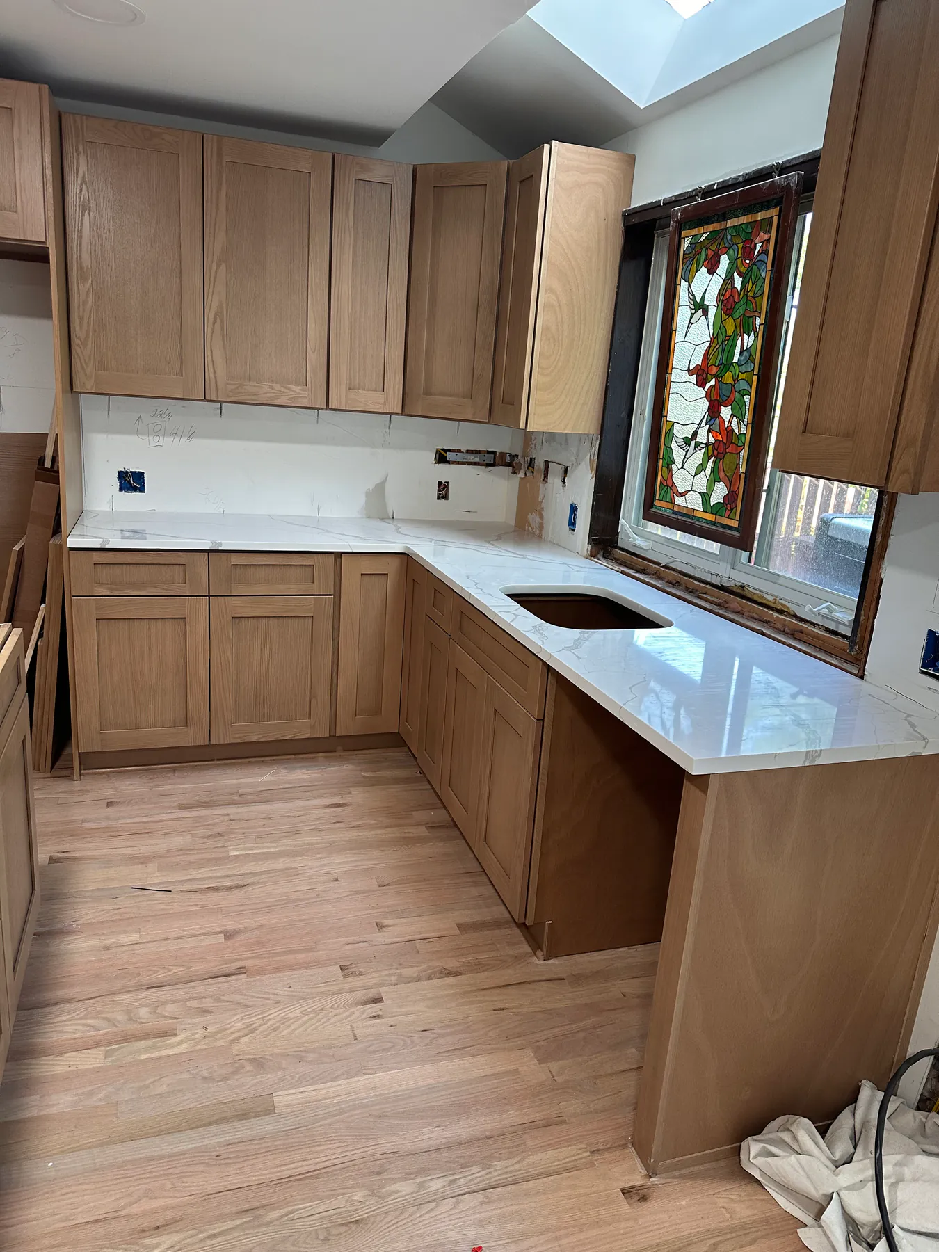 L-shaped kitchen with quartz countertops, white oak cabinetry and a stained-glass window over the sink